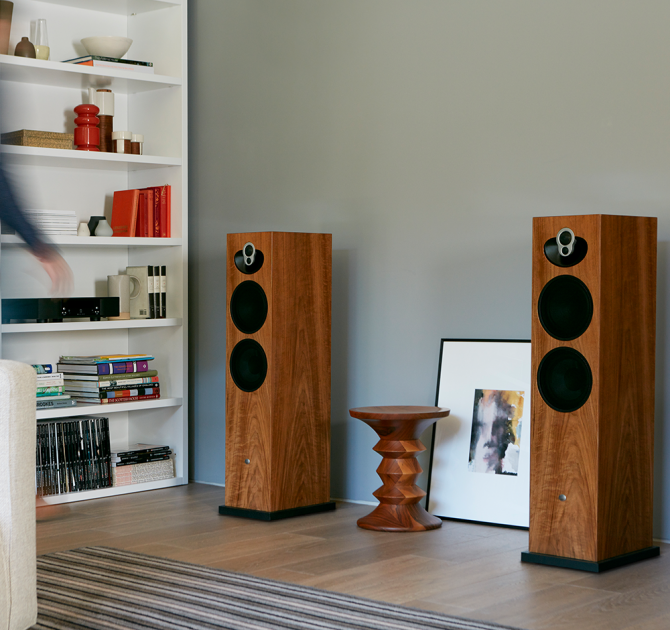 a pair Linn Majik 140 Loud Speakers with a table between them and a set of shelves to the side.