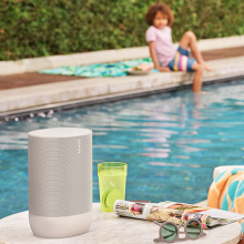 SONOS Move can be taken outside with you.  Here it's by an outside pool next to a person on a sun lounger looking at a child sitting by the pool.