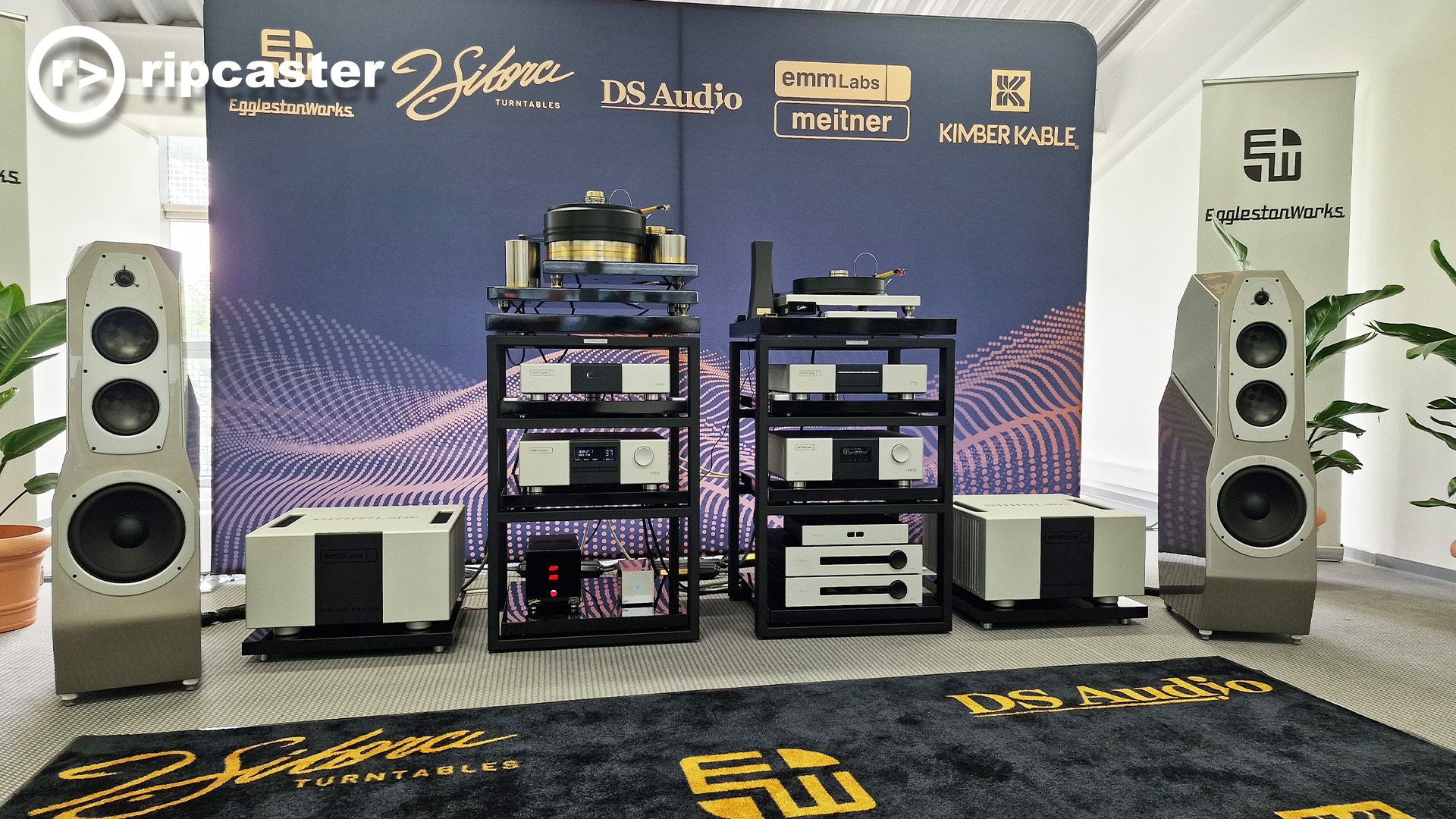 Silver floorstanding speakers either side of a load of HiFi kit in a listening room at the Munich HiFi show