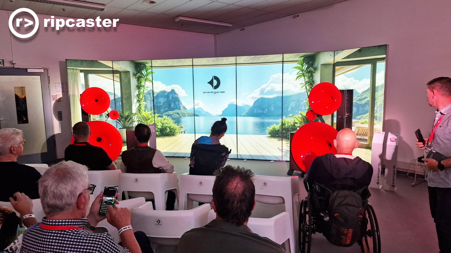 A room full of men viewed from behind.  They are listening to speakers with bright red speaker horns