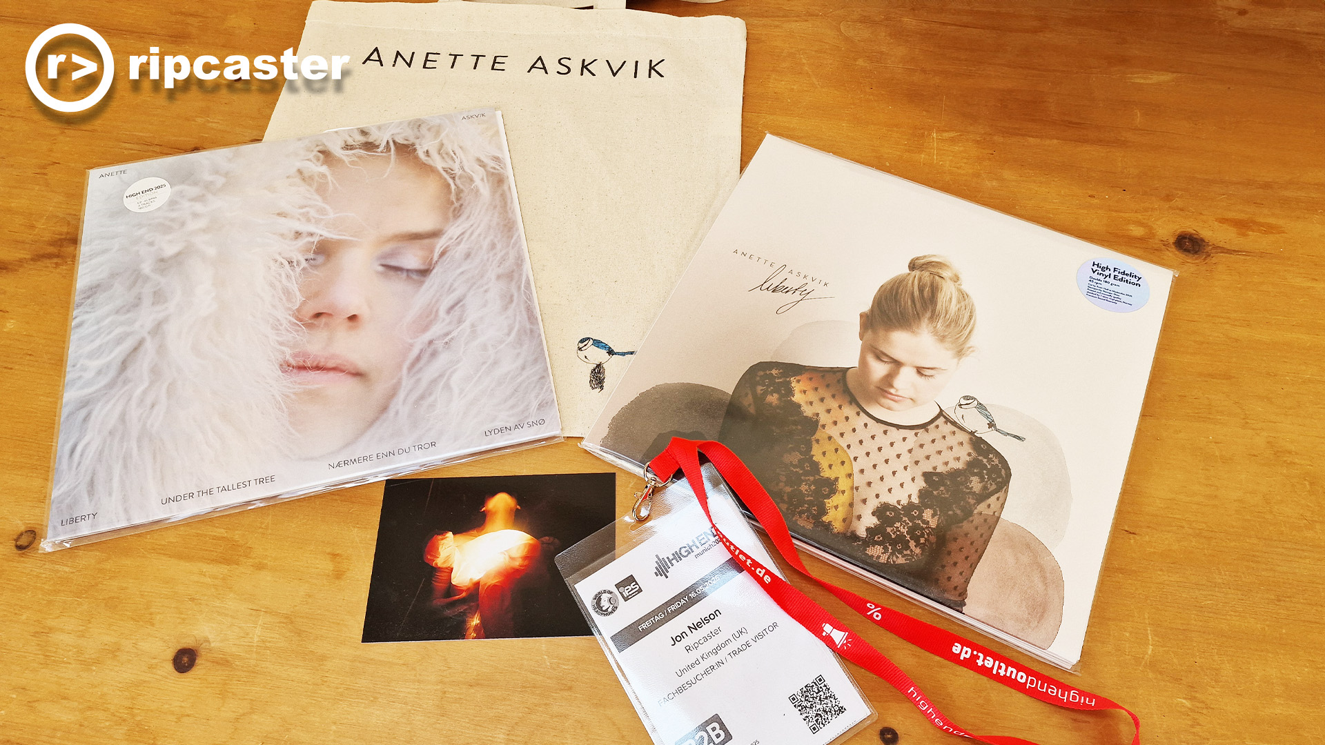 A mixture of Anette Askvik merchandise from the show along with Jon's show pass on a wooden table.  There's a tote bag along with vinyl albums and a postcard