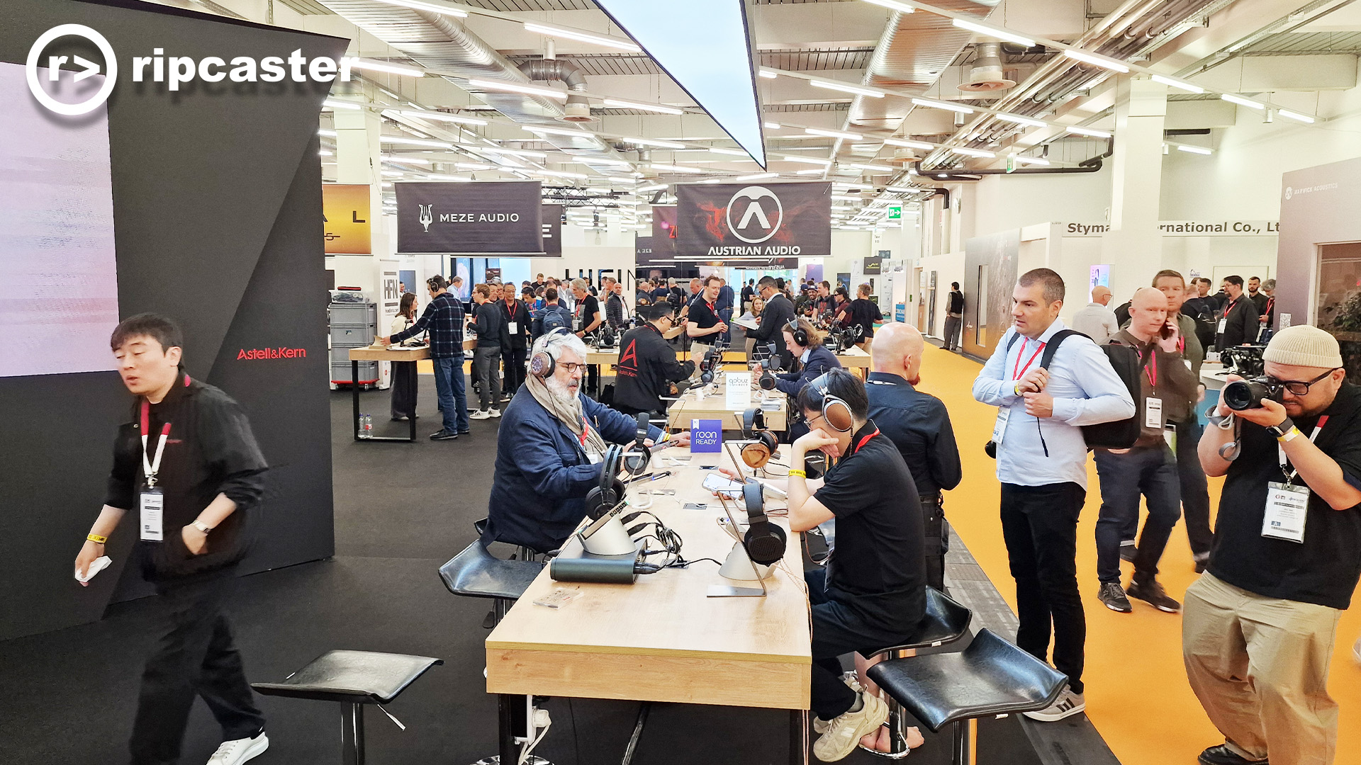 A long view of the various stands at HiFi Munich with people in view who are looking at various pieces of HiFi kit.
