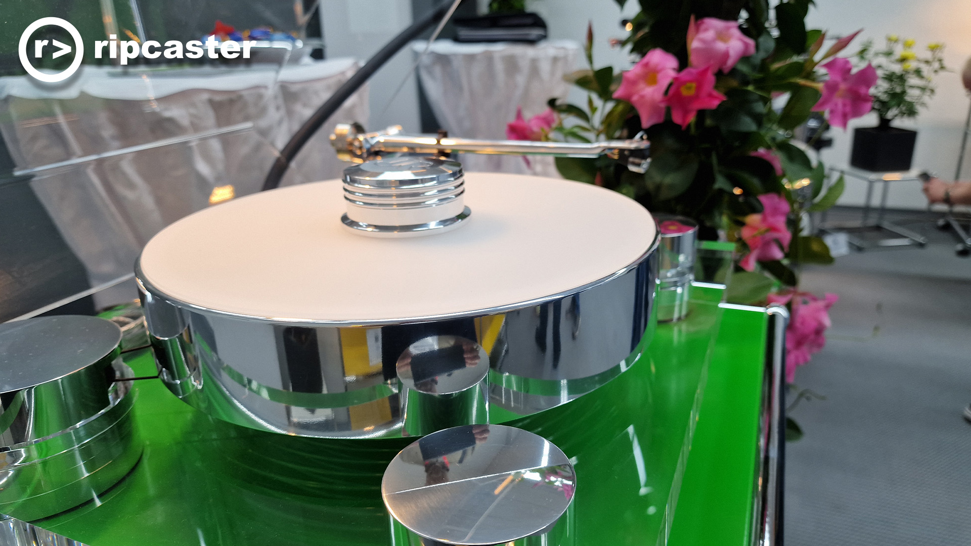 A record player on a green stand with pink flowers in the background