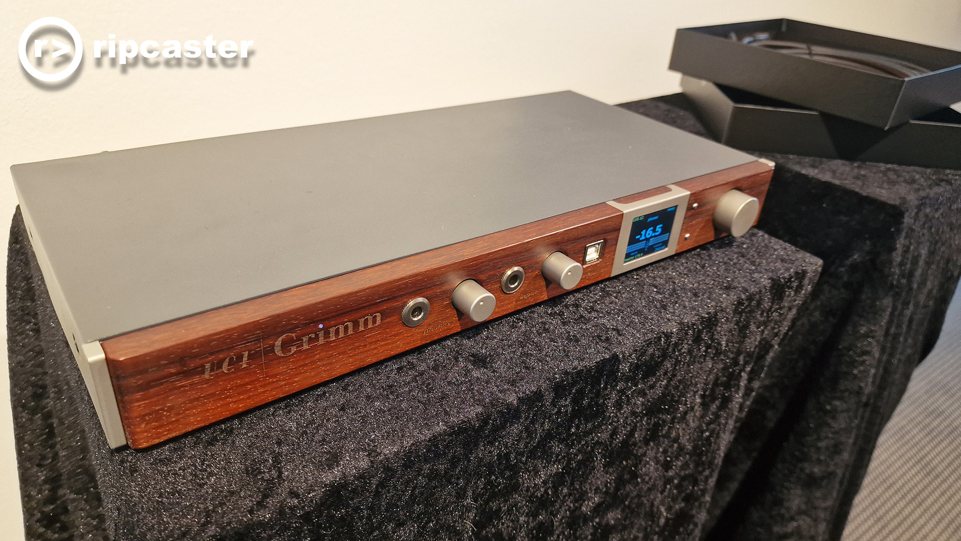 A slim piece of HiFi kit from Grimm with a wooden front panel on a stand with black fabric draped over it.