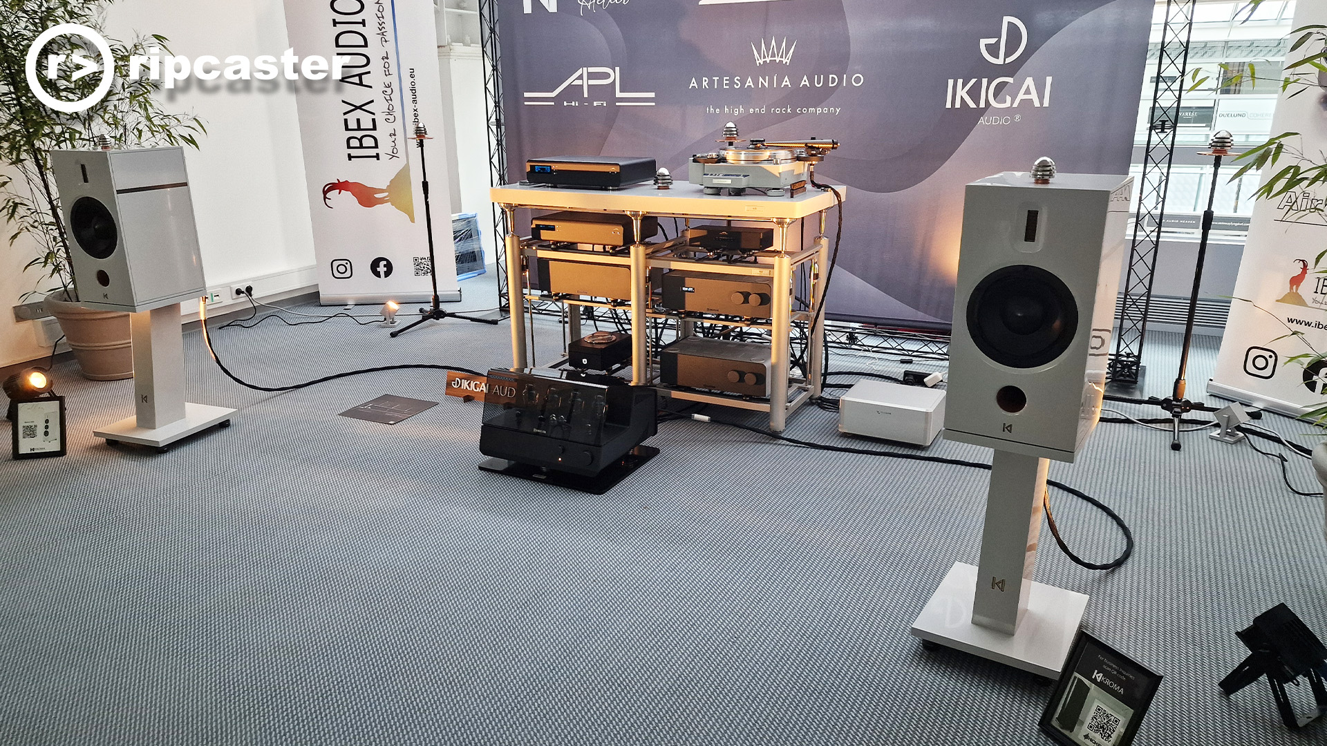 Silver speakers on stands with various bits of HiFi kit between them.