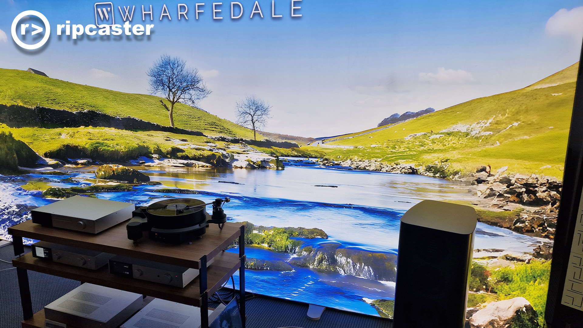 A lovely backdrop of a river running through some hills.  In front of it are some HiFi pieces of kit including a speaker and turntable.