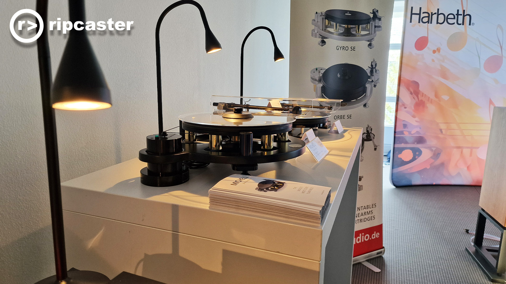 Harbeth at the Munich audio show.  A couple of turntables with small lights angled over them. and a backdrop of images of turntables.