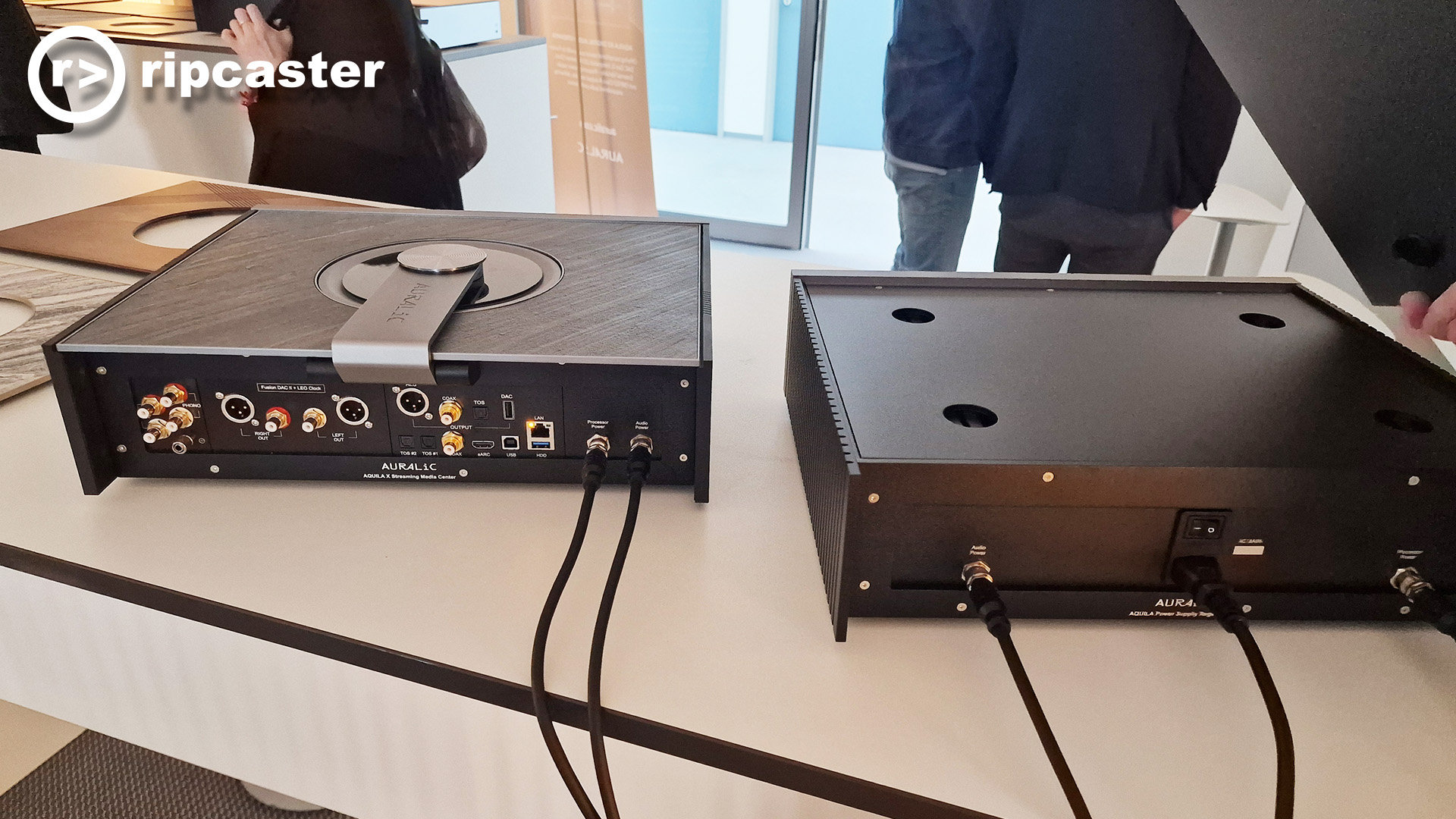 the rear of two Auralic HiFi boxes with people in the background