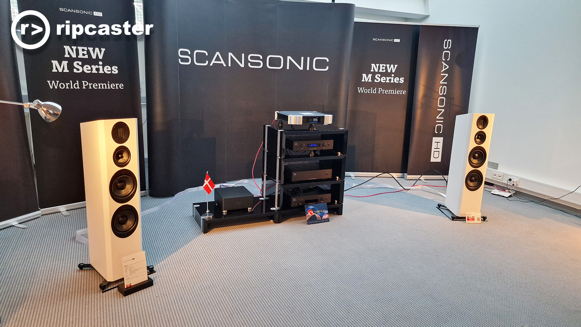 A pair of white floorstanding speakers with some HiFi kit in between them in a demo room at the HiFi show in Munich