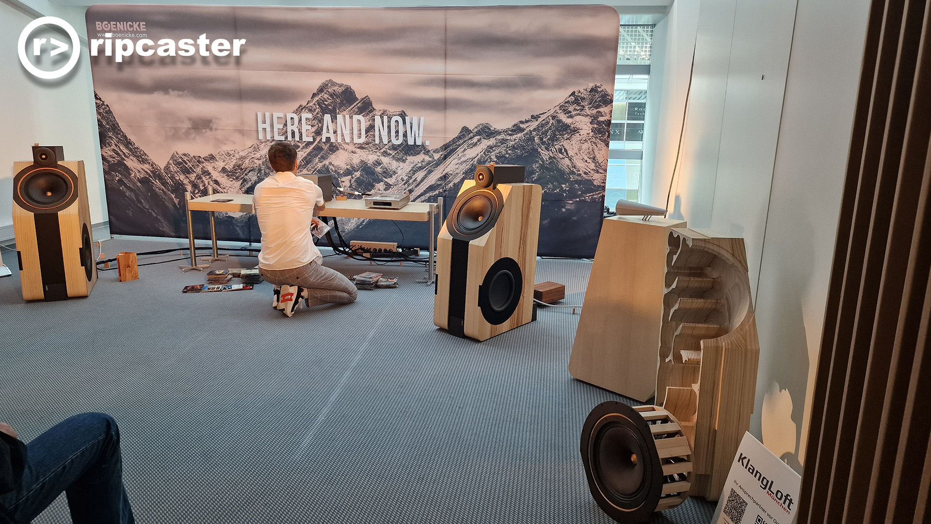 A man crouching in front of HiFi equipment.  there are wooden speakers either side of the room.