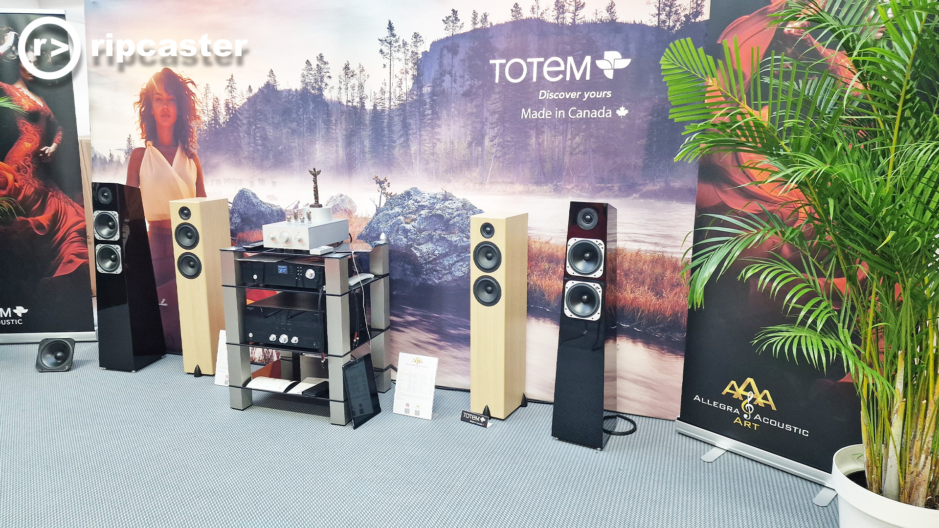 Totem room.  Floorstanding speakers with HiFi kit between them.  A large backdrop of a woman standing by a stream.