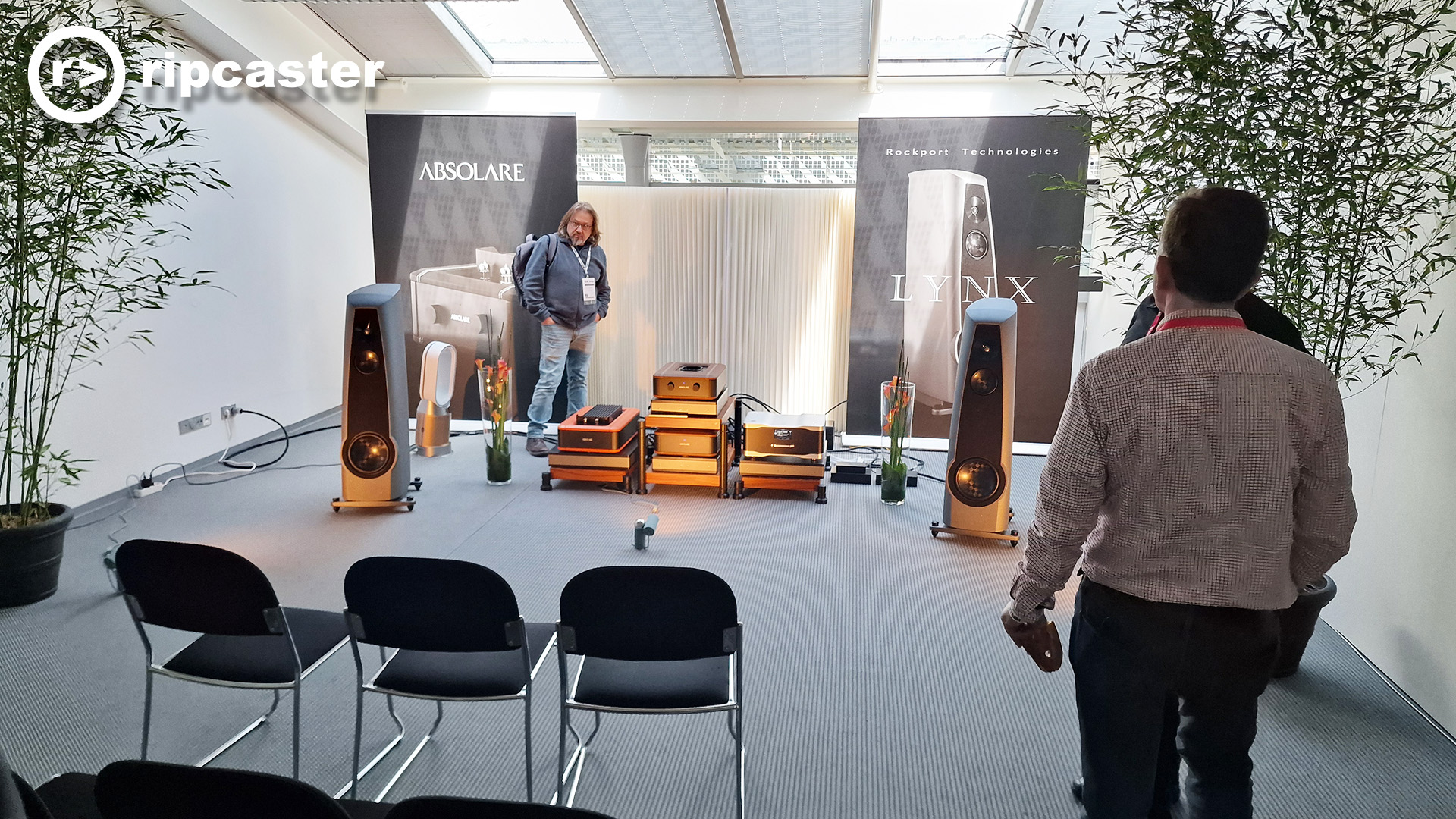 Three men in a HiFi demo room with three empty chairs facing the equipment.