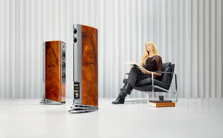 A pair of Audiovector speakers in front of a woman sitting on a black, leather chair