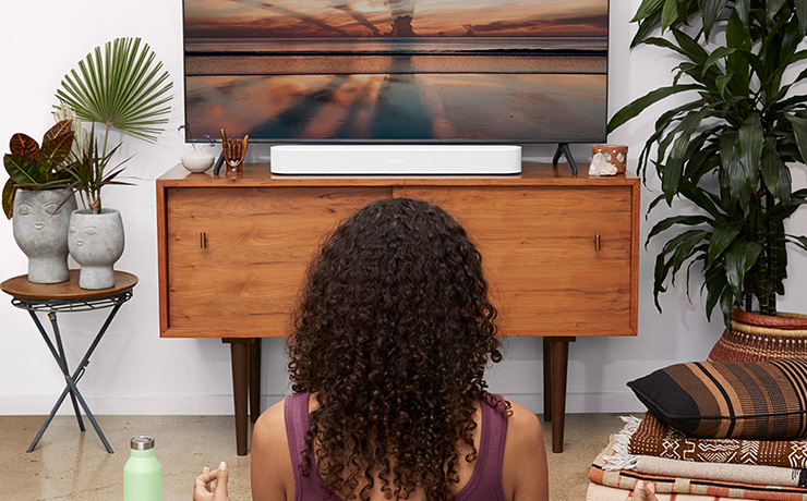 a person sitting on the floor with their back to the camera.  The beam is white and on a unit in front of the person.  On top of the unit is also a tv.