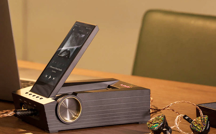 Astell & Kern Acro CA1000T in a stand with earphones on the desk beside it.