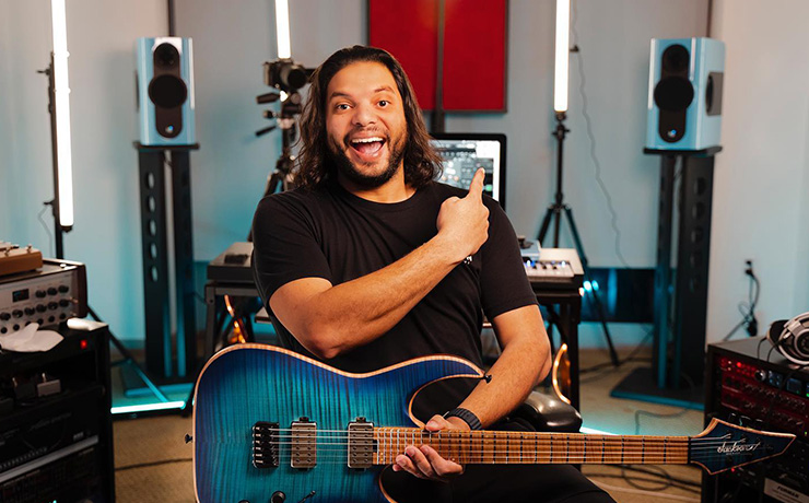 A musician with a guitar on his lap with a pair of Kii Threes in the background