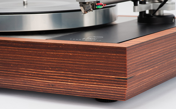 A close-up of the front right corner of an LP12 Bedrok plinth. The plinth is alternate light and dark brown