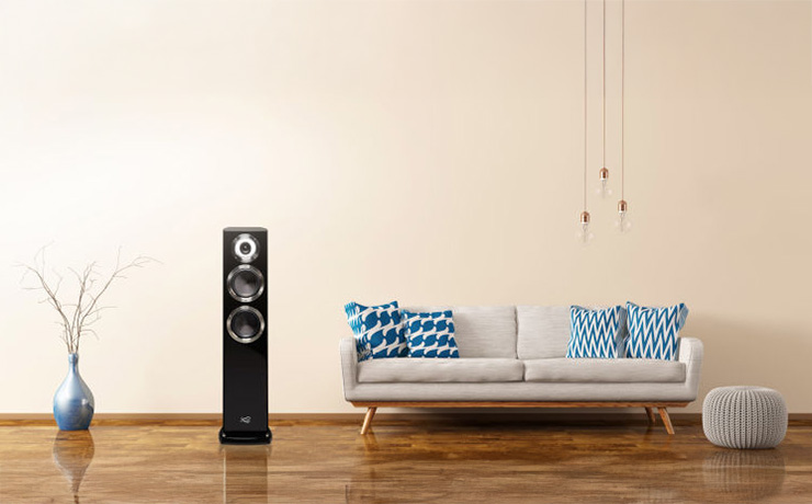 Cabasse Murano Alto floorstanding speaker in black beside a light coloured sofa with a vase the other side of it.