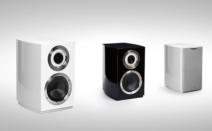 A trio of Cabasse Murano speakers. A black one in the centre and a white one either side. The white one to the left has no grille and the right one has the grille in place