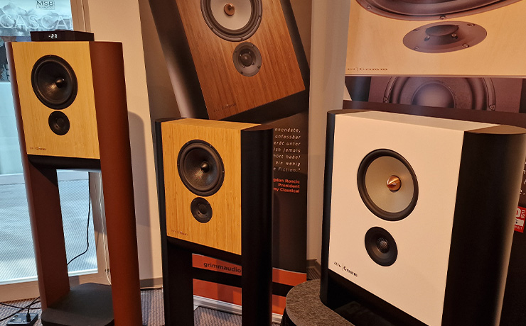 Grimm loudspeakers with the LS1be in white in the bottom right of the image. there are two other Grimm speakers to the left of the image