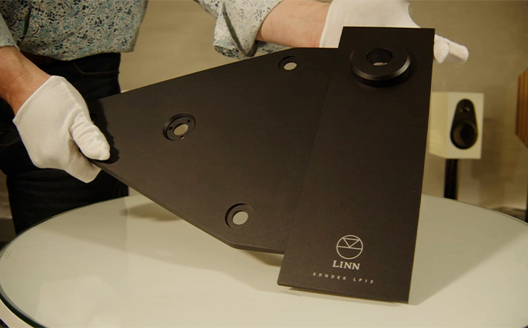 The Linn Keel SE in Jon's gloved hands being held at an angle.  There's a Linn 119 speaker in white visible in the background