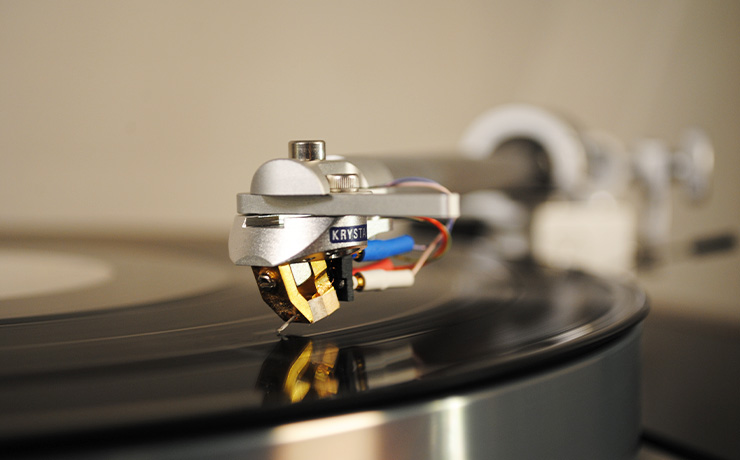 The Krystal cartridge on a tonearm.  It's on a record that's spinning.  The lighting is warm making the gold shine.