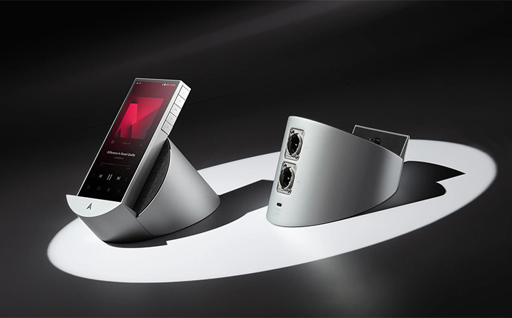 Astell & Kern PD10 sitting on its cradle with an empty cradle beside it.  On a dark background with a spotlight on both