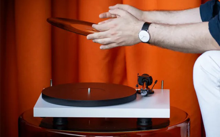 The Project EVO 2 turntable in white with a man sitting beside it holding a record. There's a dark orange curtain in the background