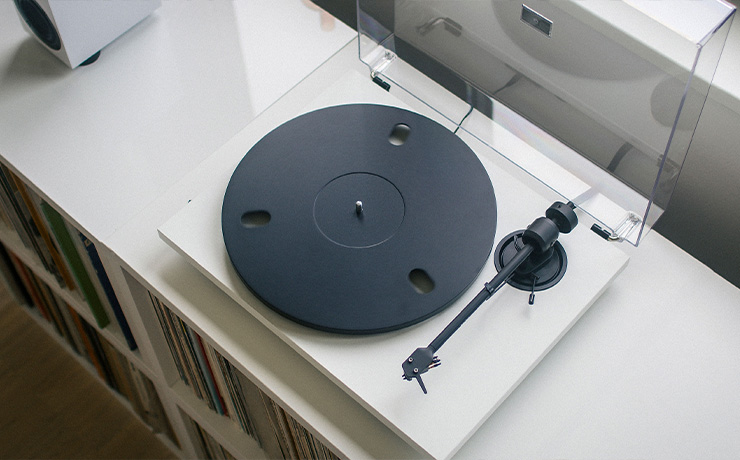 The Project E1.2 Turntable in white on top of a unit filled with vinyl
