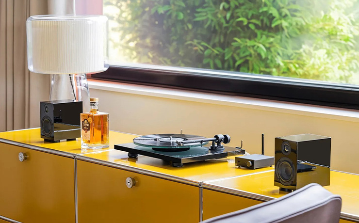 The turntable on a yellow sideboard between speakers in front of a large window