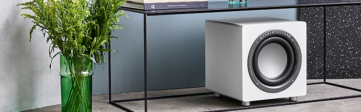 Audiovector QR Sub underneath a glass table with a vase of greenery beside it.