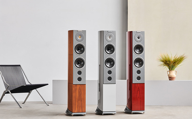 Three Audiovector R6 speakers in a light coloured room with a black chair to the left