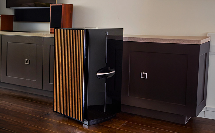 The REL 212 Black Label with wooden grille standing on a wooden floor