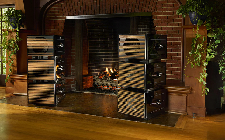 Two stacks of three REL Carbon Special Black Label Subwoofers with wooden grille either side of a large fireplace