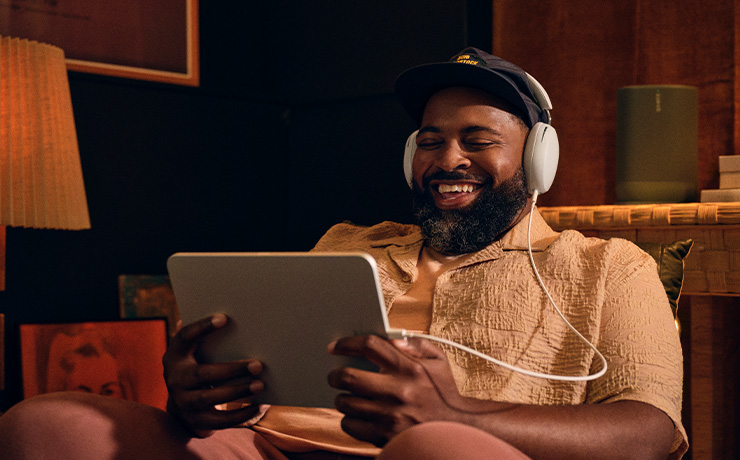 A man sitting down wearing white Sonos Ace headphones and holding a tablet