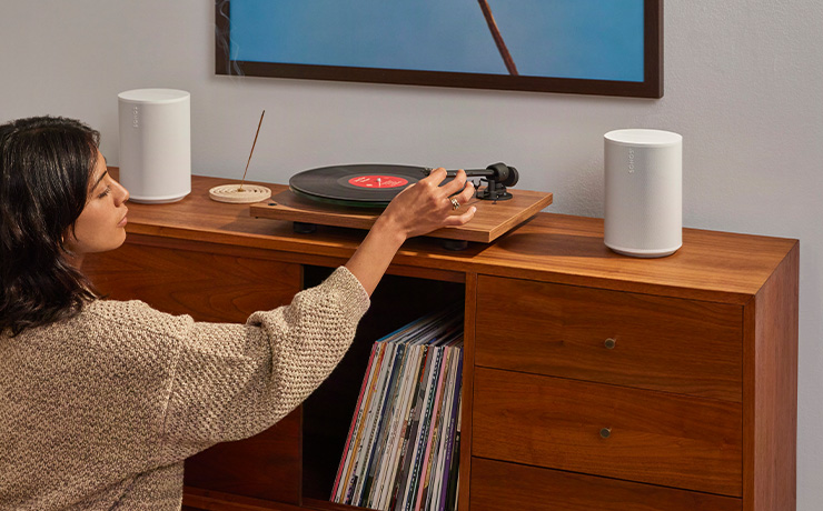 A pair of white Sonos Era 100 SL speakers on a wooden unit with a turntable between them.
