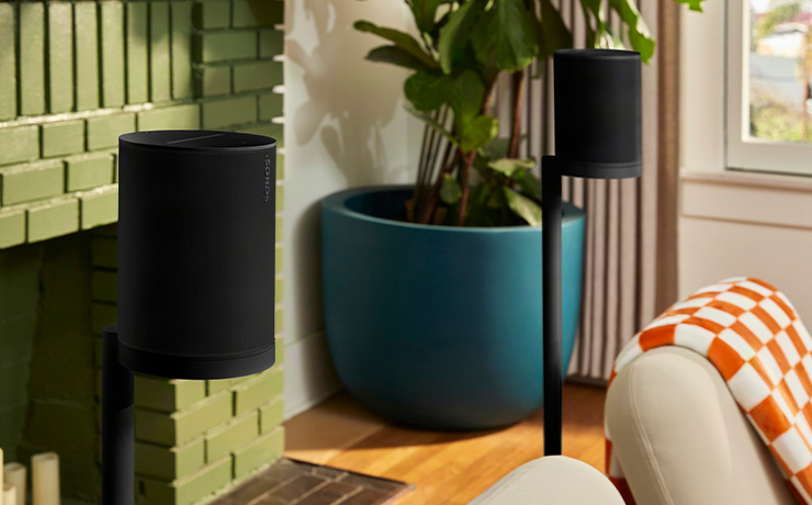 A pair of black Sonos Era 100 SL speakers on stands in a living space