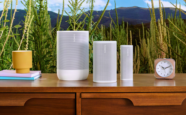 The three portable Sonos speakers in white on a table with drawers.  Left to right is Sonos Move, Play and Roam 2.