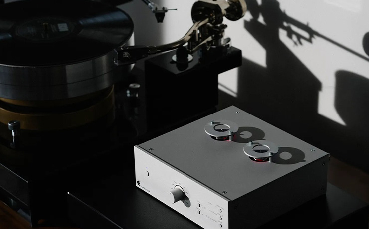 Project Tube Box DS3 B Phono Preamplifier in silver on a unit beside a turntable with the shadow of a tonearm on the wall