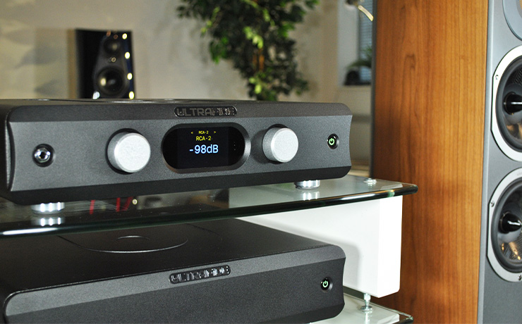 The Ultrafide U4PRE on the top shelf of a HiFi rack with the Ultrafide U500DC on the shelf below. To the right of the rack is an Audiovector floorstanding speaker and you can see the top part of a Linn 360 speaker in the background