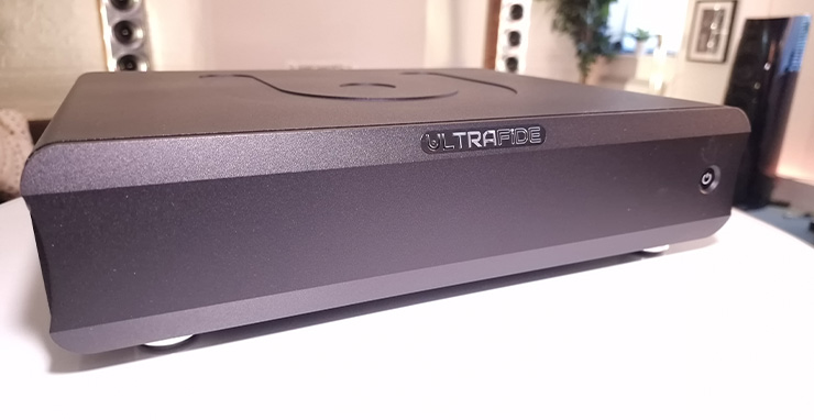 Ultrafide U500DC Audiophile Power Amplifier on a white table with three speakers spaced out in the background