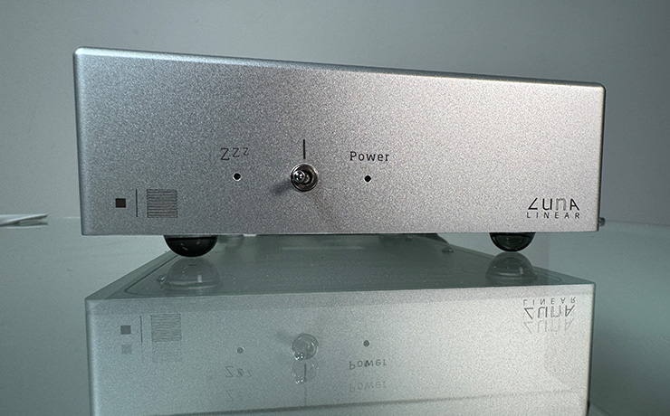 A photo of the ripcaster Vertere LunA on a glass shelf - it's silver and has from left to right, the Vertere logo, a light with "zzz" above it, the on/off switch and a light with "power" above it.  The on the bottom left it says "LunA Linear"