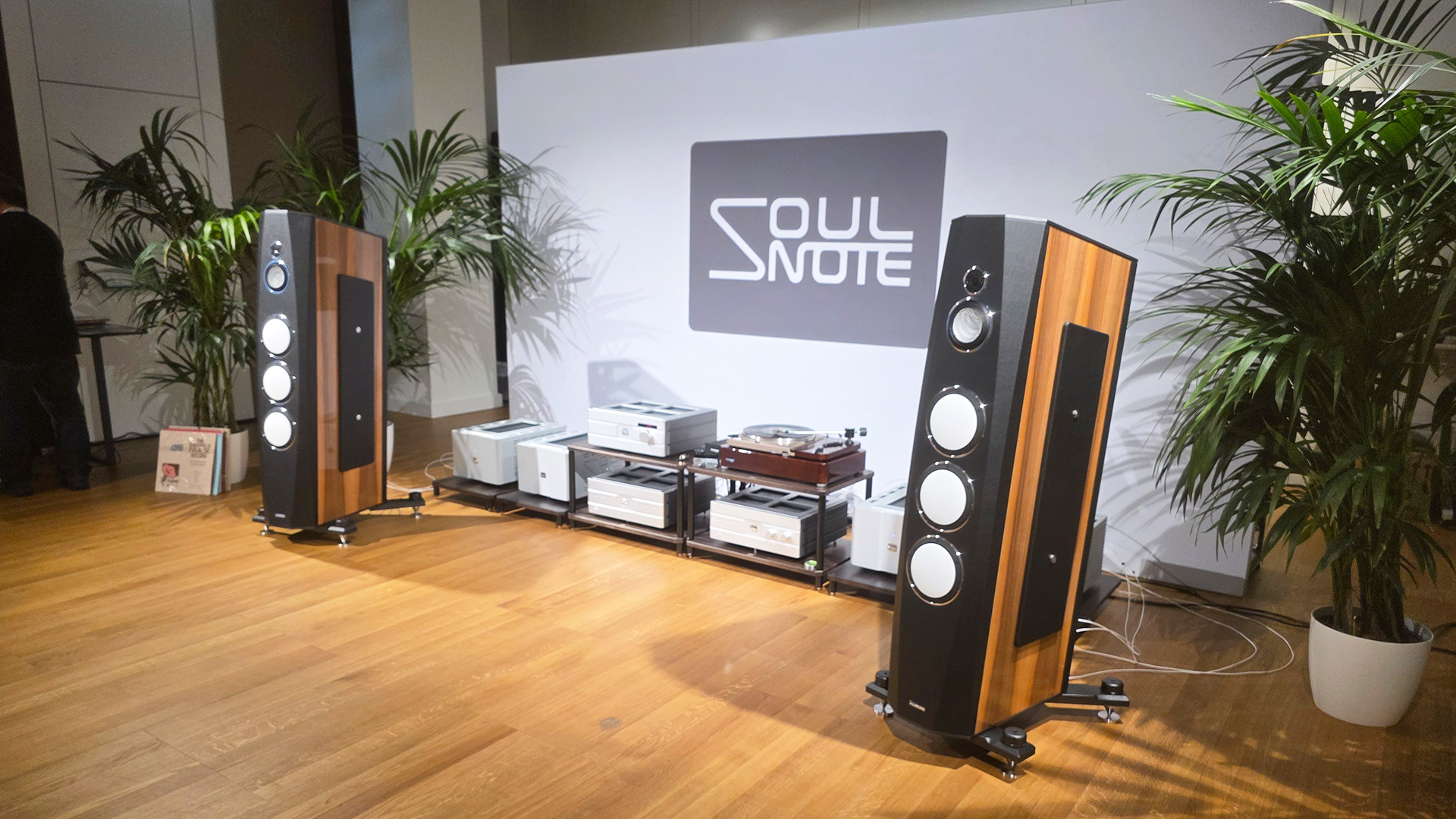 A room a the High End show in Vienna with a pair of floorstanding speakers with various pieces of audio equipment in between