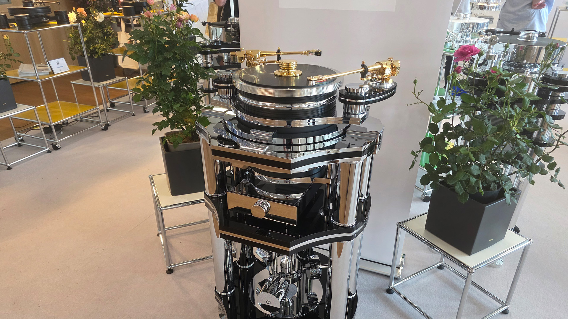 A silver and gold coloured turntable on a tall chrome HiFi unit with roses in pots either side