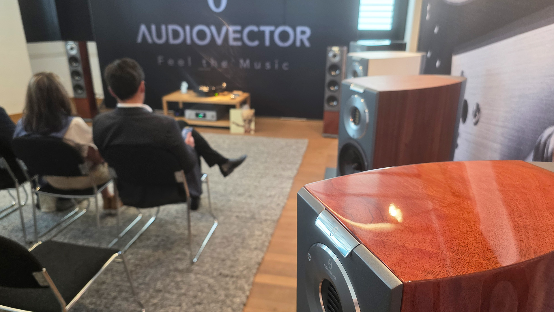The Audiovector room with speakers and the back of two people in view