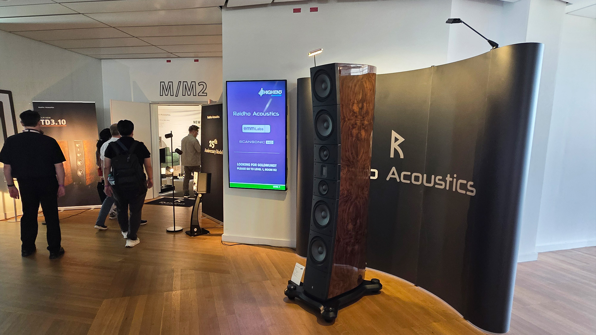A floorstanding Raidho speaker to the right with people walking to the left