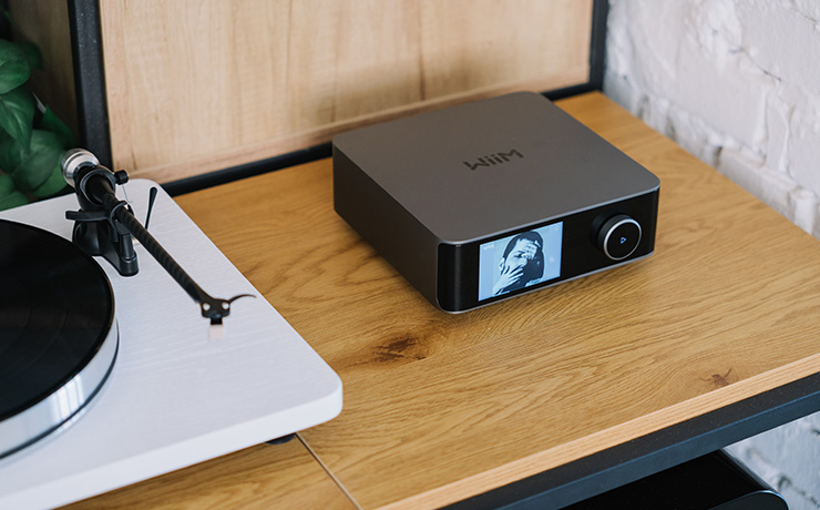 WiiM Amp Ultra on a wooden surface beside a white turntable