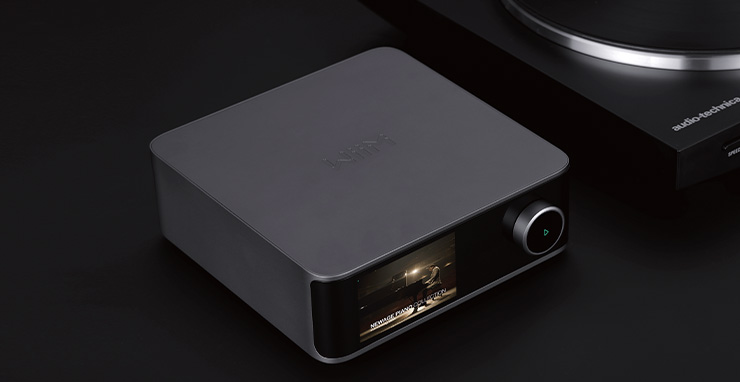 The WiiM Ultra on a black table beside a turntable. It's showing album art on the display screen.