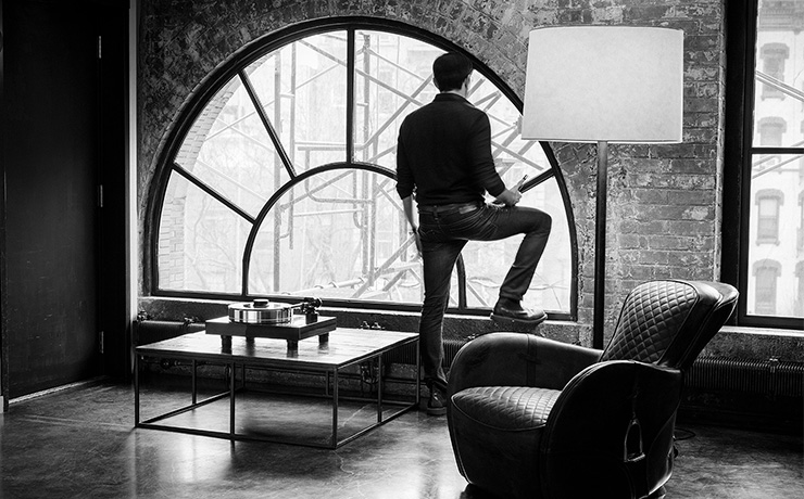 A high-rise flat with a low table with a turntable on it.  There's a man standing looking out of a large arched window