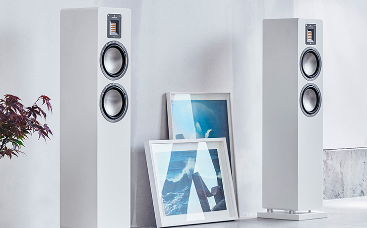 A pair of white Audiovector QR 3 SE Loudspeakers with two pictures leaning against the wall between them.